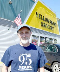 Yellowfront Grocery owner Jeff Pierce stands in front of the store, which is celebrating its 95th anniversary. His shirt - a gift from a customer - reads “It took me 95 years to look this good.” (Maia Zewert photo)