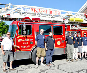 From left: Assistant Fire Chief Nick Merry, James Pray, Kevin Brewer, Kyle Viele, Devin Grover, Steven Smith, Capt. Nick Grover, Brycson Grover, and Chris Cossette stand in front of Ladder 1 on Monday, July 4. The truck is back in service after nearly a year away for repairs. (Charlotte Boynton photo)