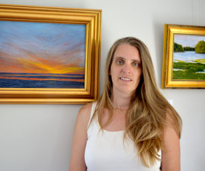 Pemaquid Watershed Association Executive Director Jennifer Hicks is flanked by two of Helen Warner's oil paintings that are part of Warner's show, "Our Natural World," currently hanging on the walls of the PWA's new office at 584 Main St., Damariscotta. At left is "Morning"; on the right is "Looking Upstream." (Christine LaPado-Breglia photo)