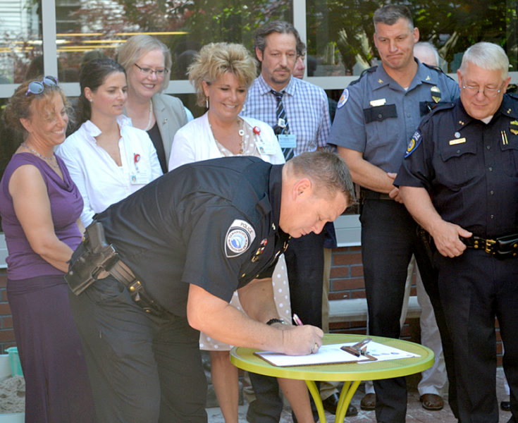 Damariscotta Police Chief Ron Young signs a memorandum of understanding for the Lincoln County Recovery Collaborative as fellow police chiefs and stakeholders from LincolnHealth, Mid Coast Hospital, and the CLC YMCA look on Friday, July 15. (Abigail Adams photo)