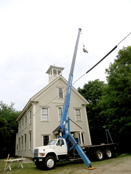 A crane lifts Shawn Hickey and the newly restored weather vane to assist the waiting Michael Alderson at the top of the cupola of the Washington School in Round Pond on Thursday, Aug. 18. (Haley Bascom photo)