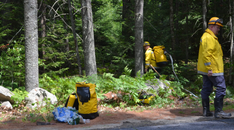 Firefighters walk packs of booster hoses to the scene of a brush fire in a wooded lot on Willow Lane in Wiscasset the afternoon of Monday, Aug. 8. (Abigail Adams photo)