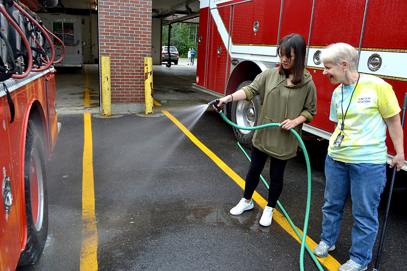 Lincoln Academy sophomore Gloria Tian (left) sprays down a Damariscotta fire truck as LA math teacher Libby Mooney looks on. Students in Lincoln Academy's sophomore class did community service in Damariscotta and Newcastle as part of Lincoln Academy's annual Sophomore Service Day on Wednesday, Aug. 31. (Maia Zewert photo)