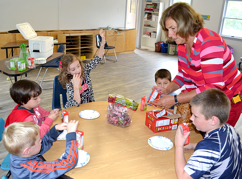 Terry Mitchell, the director of South Bristol SchoolÂ’s new after-school program, serves snacks to the five children who attended the program Tuesday, Sept. 6. Clockwise from bottom left: South Bristol kindergartners Sam Kress and Autumn Cantillo, third-grader Maya Redonnett, kindergartner Robert Bennett, and third-grader Blake Gamage. (Maia Zewert photo)