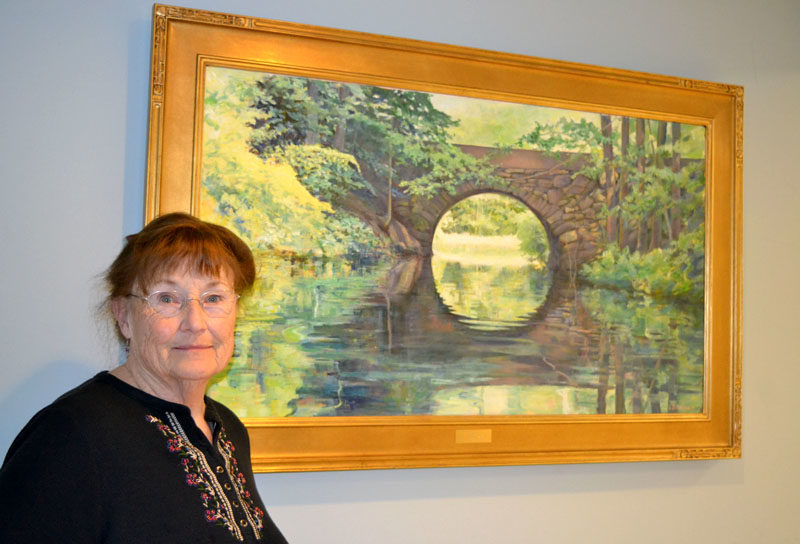 Miles Memorial Hospital League Art Committee President Julie Babb stands before "Sanctuary," an oil painting of the Benner Road Stone Arch Bridge over the Pemaquid River painted by and donated to LincolnHealth - Miles Campus by Damariscotta artist Bertil Whyman earlier this year. (Christine LaPado-Breglia photo)