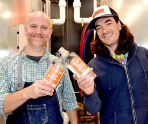Split Rock Distilling co-founders Matt Page (left) and Topher Mallory display bottles of white whiskey, the newest spirit in the organic distillery's line. The Newcastle business will celebrate its grand opening throughout Columbus Day weekend, Oct. 7-9. (Maia Zewert photo)