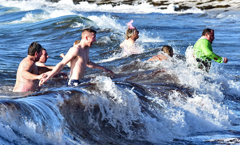 A wave overtakes some of the participants in the Pemaquid Polar Bear Dip. (Photo courtesy Sherrie Tucker/sherrietucker.com)