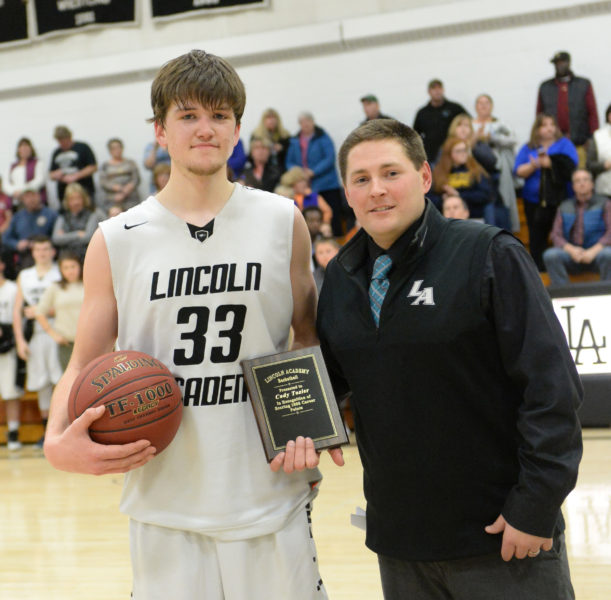 Lincoln Academy boys basketball coach Ryan Ball presented senior Cody Tozier with the game ball and a plaque in honor of his scoring his 1,000th career point on Feb. 2. (Paula Roberts photo)