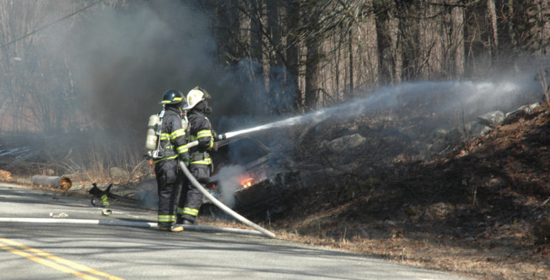 Firefighters work to prevent a car fire from spreading to the nearby woods on South Clary Road in Jefferson. (Alexander Violo photo)