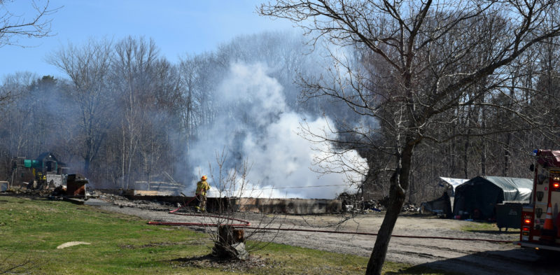 A firefighter douses the remains of a building on Pension Ridge Road in Boothbay the morning of Saturday, April 15. (J.W. Oliver photo)