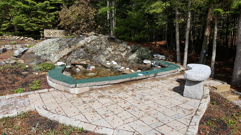 A patio with a water feature incorporating natural ledge on a property in Boothbay, designed and built by C.J. Turner. The water feature uses a reservoir and a pump to recirculate the water. (Photo courtesy C.J. Turner)