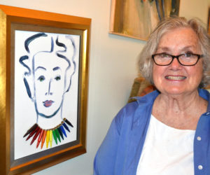 Franciska Needham stands beside an earlier self-portrait that hangs inside her home, which is adjacent to her Water Street art gallery. Needham said she added the rainbow-colored bullet necklace "because no matter where I was in the world, they'd know I was American, because we're gun people." (Christine LaPado-Breglia photo)