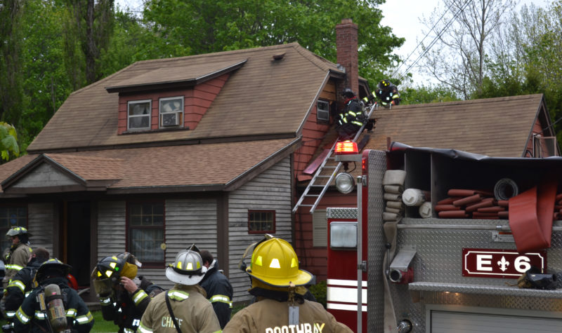 Firefighters cut out an area of roof and wall around the chimney of a Flood Avenue home to prevent the spread of a fire the afternoon of Monday, May 22. (Abigail Adams photo)