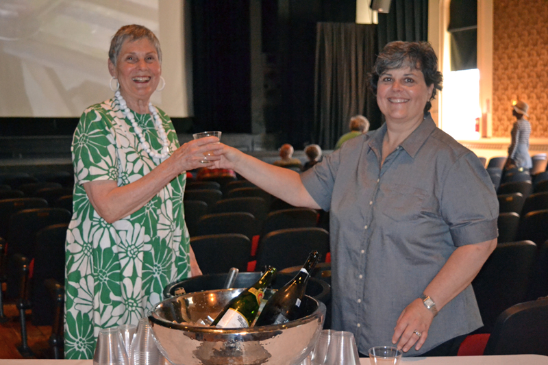Lincoln Theater member Janet Elwin (left) accepts a glass of prosecco from Sarah Maurer, who poured drinks for attendees during the June 20 open house at Lincoln Theater in Damariscotta celebrating the theater's newly restored vintage windows. (Christine LaPado-Breglia photo)