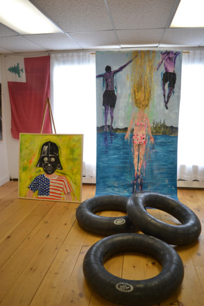 A huge painting of kids jumping into water, complemented by a trio of inner tubes, stands to the right of "The Farce is with You," at Michael Blaze Petan's current show in the West Gallery of River Arts in Damariscotta. (Christine LaPado-Breglia photo)