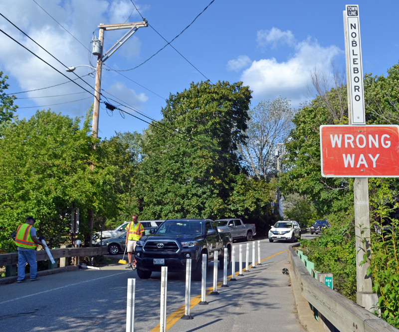 A truck drives over the Damariscotta Mills bridge Sunday, Aug. 20 as Newcastle Selectman Ben Frey (left) and Road Commissioner Steve Reynolds install traffic bollards. (Maia Zewert photo)