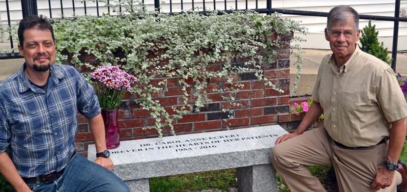 The late Dr. Carol Eckert's son, Sam Frankel (left), and husband, Jeff Frankel, kneel on either side of a bench the Sheepscot Valley Health Center dedicated to her memory Tuesday, Aug. 15. (Abigail Adams photo)