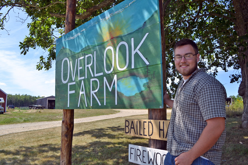 Ridge Barnes stands next to the sign for Overlook Farm. Barnes is the fifth generation of the Barnes family to run the farm. (Charlotte Boynton photo)