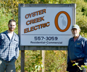 Daniel Baty (left) and Al Monaco stand in front of the sign for Oyster Creek Electric at 629 Bristol Road. Monaco is selling the business to Baty, his employee of four years. (Maia Zewert photo)