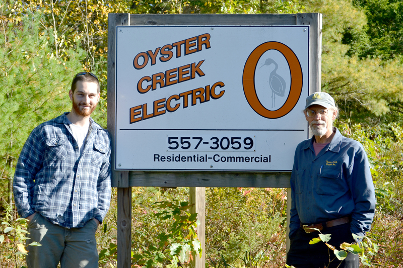 Daniel Baty (left) and Al Monaco stand in front of the sign for Oyster Creek Electric at 629 Bristol Road. Monaco is selling the business to Baty, his employee of four years. (Maia Zewert photo)