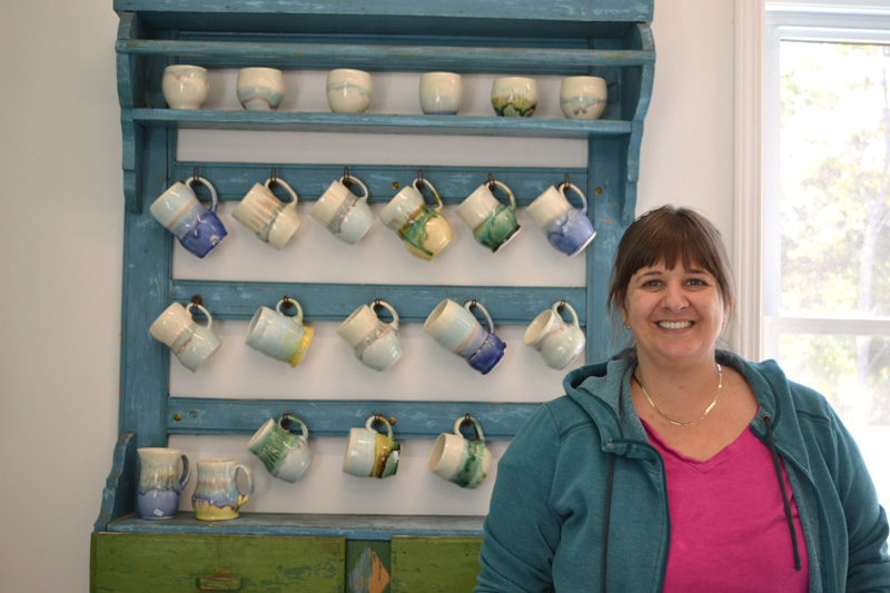 Liz Proffetty stands in the retail area of Neighborhood Clay, near a rack of ceramic mugs she created. (Christine LaPado-Breglia photo)