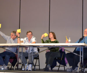 From left: Whitefield Selectmen Tony Marple, Lester Sheaffer, Charlene Donahue, and Frank Ober raise their cards to vote for a 180-day moratorium on marijuana establishments during a special town meeting at Whitefield Elementary School on Wednesday, Dec. 6. (Christine LaPado-Breglia photo)