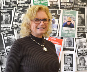 Village Optical owner Jane Hall stands in front of a wall of her clients' photos in the business at Main Street Centre in Damariscotta. The business will close March 31 after 29 years. (Maia Zewert photo)