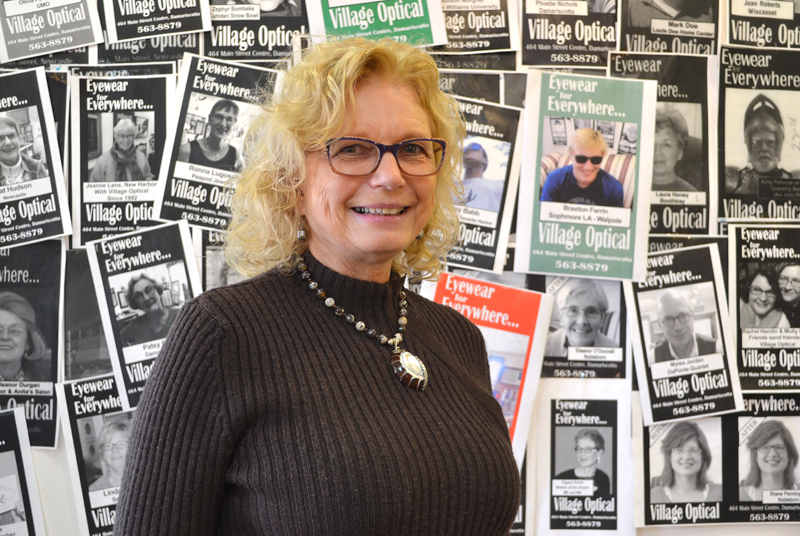 Village Optical owner Jane Hall stands in front of a wall of her clients' photos in the business at Main Street Centre in Damariscotta. The business will close March 31 after 29 years. (Maia Zewert photo)