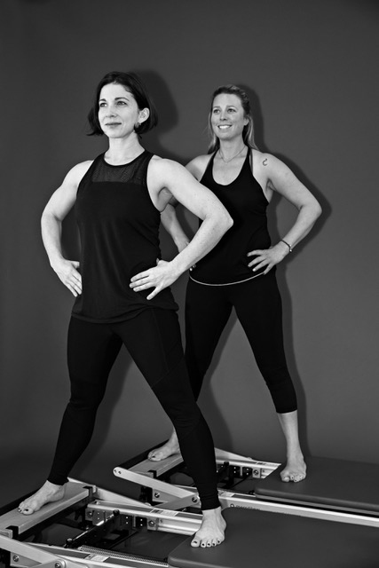 Coaches Darcy Fraser (left) and Virginia Shaw demonstrate the side split on Pilates Reformers.