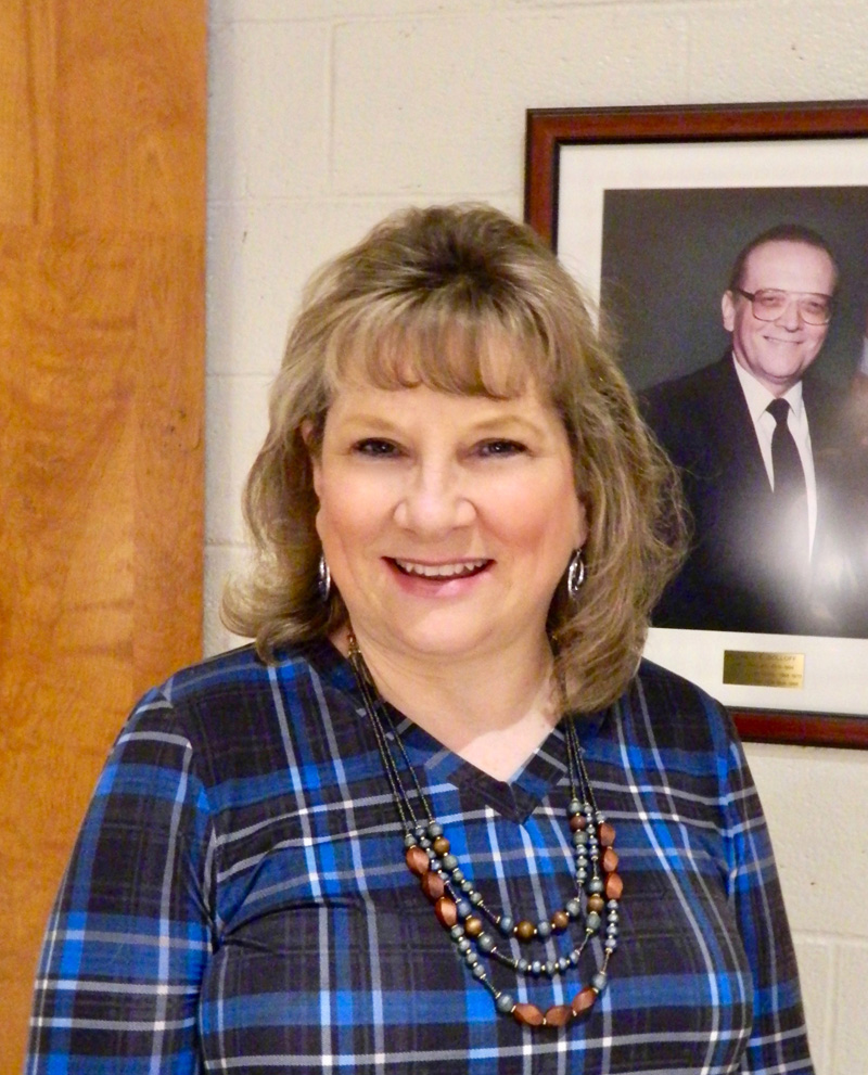 Linda Pease poses in front of a photo of her father, the late Ronald Doloff, Medomak Valley High School principal from 1970-1994. Pease will begin the same job in July after six months in an acting role. (Photo courtesy Lisa Genthner Gunn)