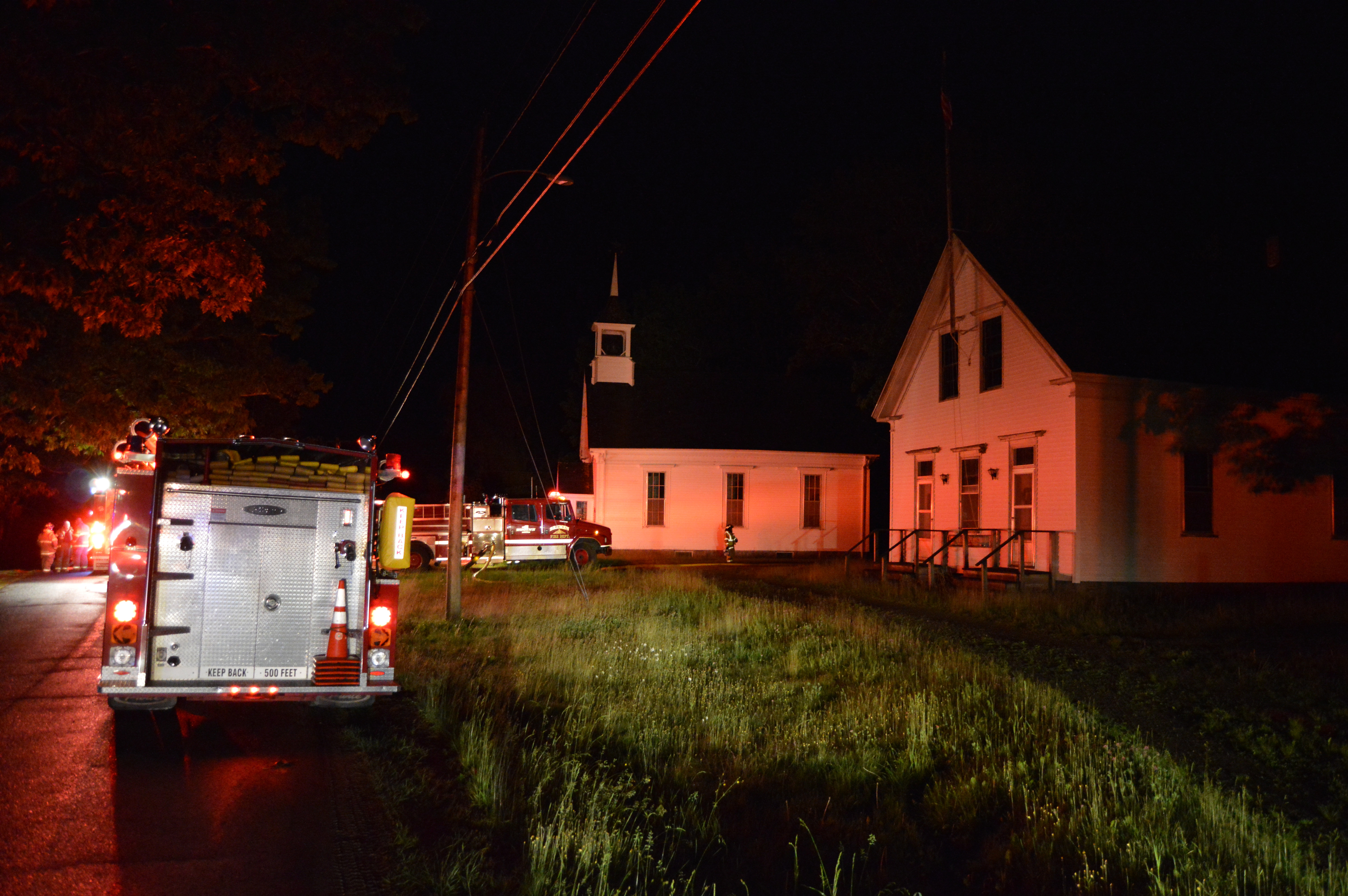 Firefighters and trucks at the scene of a fire on Dutch Neck Road in Waldoboro late Thursday, June 14. The buildings visible are the historic St. Paul's Union Chapel and Dutch Neck Schoolhouse. The fire was at a house on a driveway behind those buildings. (J.W. Oliver photo)