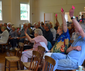 Westport Island voters raise their cards in favor of an article during annual town meeting at the historic town hall Saturday, June 23. Fifty-six voters attended the meeting. (Charlotte Boynton photo)
