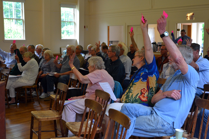 Westport Island voters raise their cards in favor of an article during annual town meeting at the historic town hall Saturday, June 23. Fifty-six voters attended the meeting. (Charlotte Boynton photo)