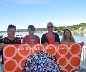 From left: kNOw S.U.P. members Ali Stevenson, Jenny Mayher, Adele Gale, and Co-chair Eleanor Kinney hold a painting on the deck outside the organization's meeting place in downtown Damariscotta. The painting illustrates the group's mission to reduce reliance on single-use plastics. (Jessica Clifford photo)