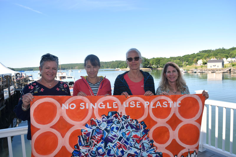 From left: kNOw S.U.P. members Ali Stevenson, Jenny Mayher, Adele Gale, and Co-chair Eleanor Kinney hold a painting on the deck outside the organization's meeting place in downtown Damariscotta. The painting illustrates the group's mission to reduce reliance on single-use plastics. (Jessica Clifford photo)