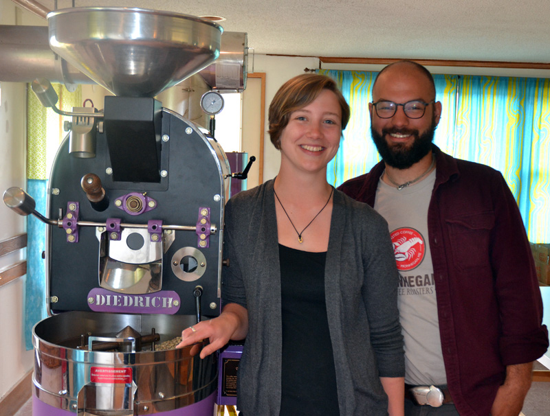 Monhegan Coffee Roasters co-owners Carley Mayhew and Mott Feibusch stand next to their coffee roaster in the business's headquarters on Monhegan Island. (Maia Zewert photo)