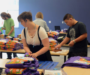 From left: Lincoln Academy volunteers Keith Grant, Becca Lambert, and Muyao Sun fold 2018 Pumpkinfest T-shirts in the Lincoln Academy ATEC building.