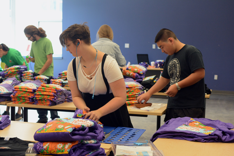 From left: Lincoln Academy volunteers Keith Grant, Becca Lambert, and Muyao Sun fold 2018 Pumpkinfest T-shirts in the Lincoln Academy ATEC building.