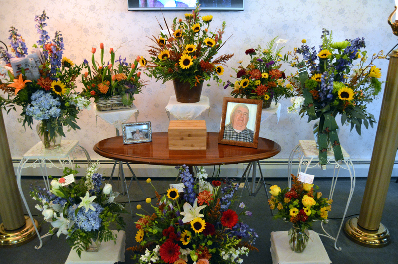 A display of flowers and photos in memory of Samuel E. "Sam" Roberts, publisher emeritus of The Lincoln County News, at the Strong-Hancock Funeral Home in Damariscotta on Thursday, Nov. 15. The bouquet at left holds the Nov. 8 edition of the newspaper, the bouquet at right a pair of his trademark suspenders. (J.W. Oliver photo)