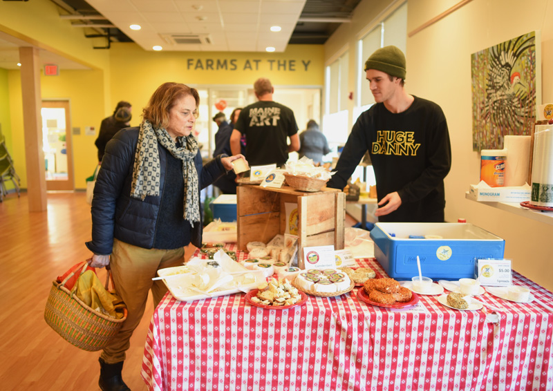 Daria White, of Damariscotta, looks at cheese from Appleton Creamery as employee George Hill mans the creamery's table at the farmers market at the CLC YMCA in Damariscotta, Friday, Nov. 30. (Jessica Picard photo)