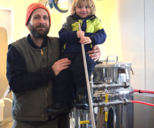 Kyle DePietro, co-owner of Sasanoa Brewing, holds his son, Stellan DePietro, in the building where he brews beer at Tarbox Farm. (Jessica Clifford photo)