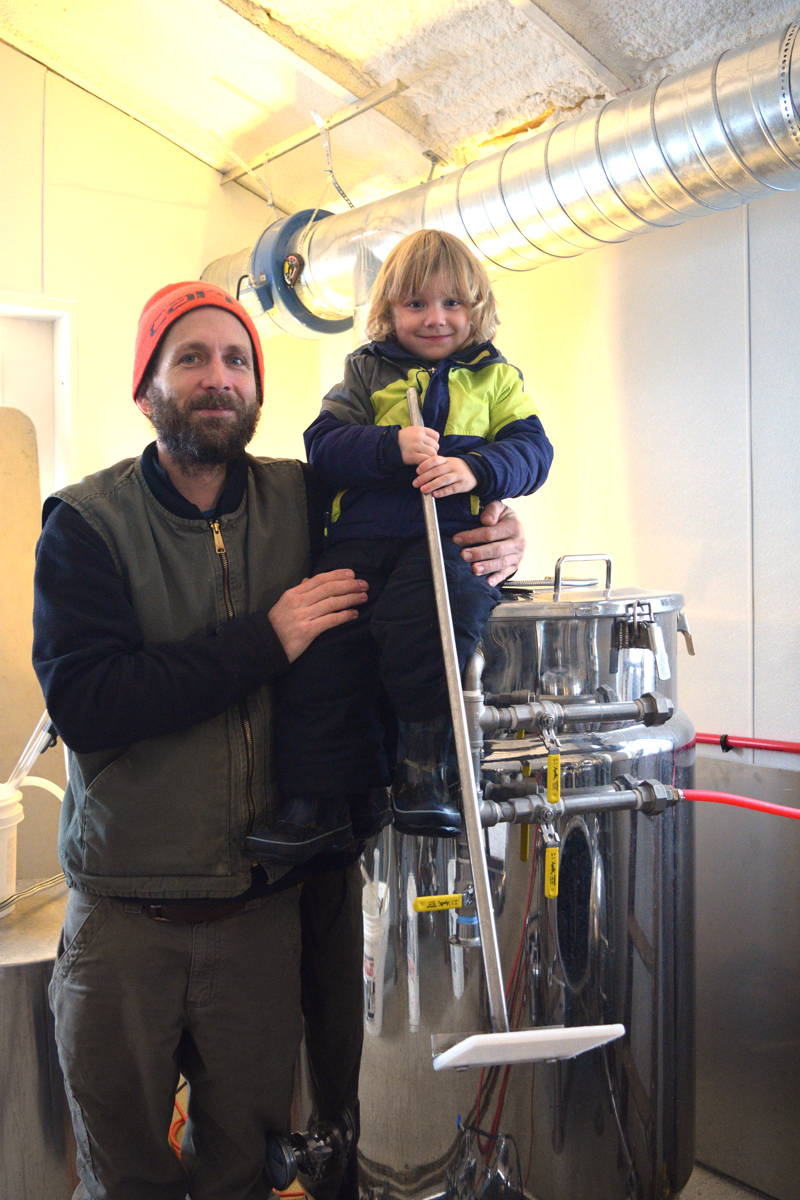 Kyle DePietro, co-owner of Sasanoa Brewing, holds his son, Stellan DePietro, in the building where he brews beer at Tarbox Farm. (Jessica Clifford photo)