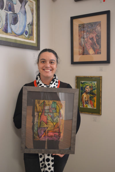 Rachel Walls, owner of Rachel Walls Fine Art in Cape Elizabeth, holds one of artist Cabot Lyford's earliest works, from the 1940s. Two more works from the same time period hang on the wall at right. (Christine LaPado-Breglia photo)