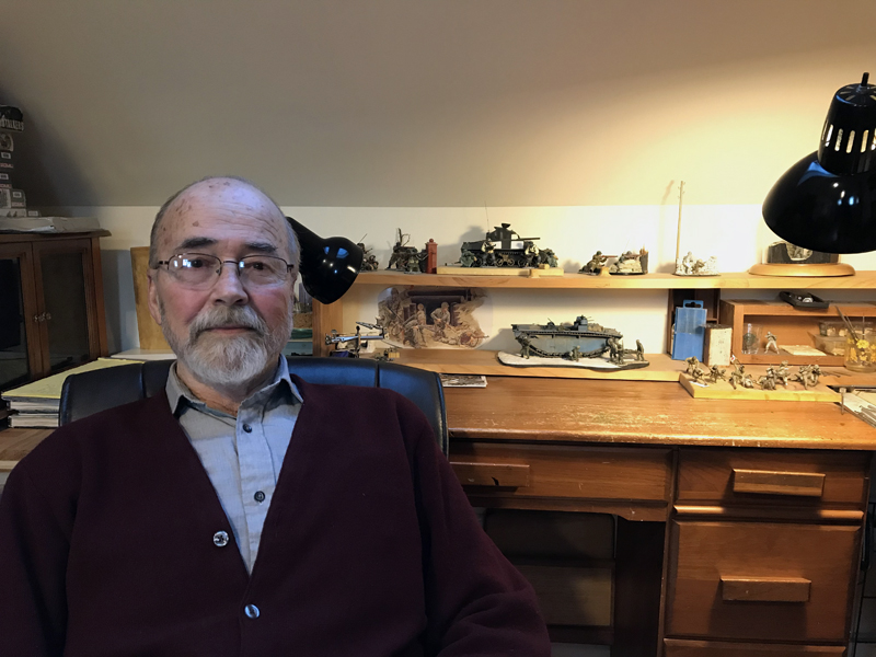 Ed Strausberg sits next to parts of an incomplete diorama of Saipan on his desk at his home in Round Pond. Unable to complete the work due to a tremor, he hopes to find someone willing to finish the job. (J.W. Oliver photo)