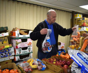 Earl Lemieux hands a bag of carrots and onions to a client at the St. Denis Food Pantry in Whitefield on Friday, March 1. Earl Lemieux and his late wife, Mary Lemieux, started the pantry more than 20 years ago. (Jessica Clifford photo)