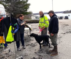 From left: Erin Lally, a representative of Lifejackets for Lobstermen, shows a personal flotation device to lobstermen Gary Clifford (with Maggie) and Brad Burns at Round Pond Landing on May 7. (Candy Congdon photo)