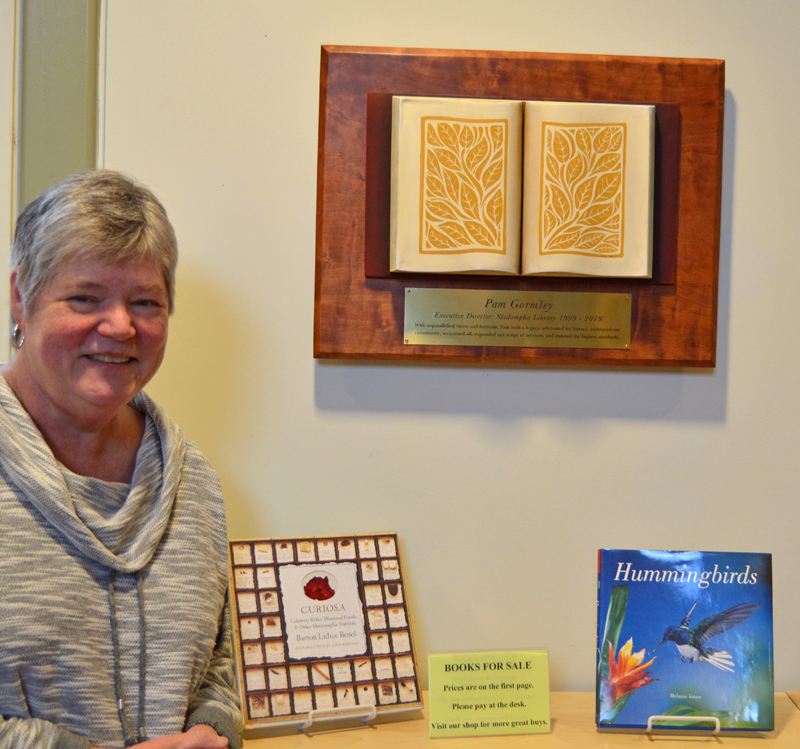 Skidompha Library Executive Director Pam Gormley stands next to her retirement gift, a plaque and sculpture by Damariscotta artist Jaques Vesery. (Evan Houk photo)