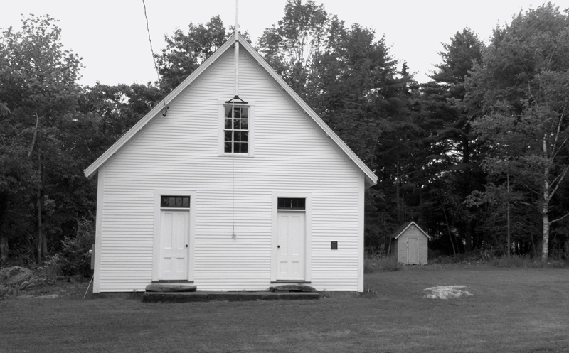 The S Road Schoolhouse and the old smokehouse on the edge of the woods to the right of the building.