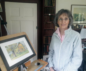 Lucy Martin, in her Whitefield home studio/library with one of her watercolor paintings, which will be exhibited in July at Sheepscot General Store.