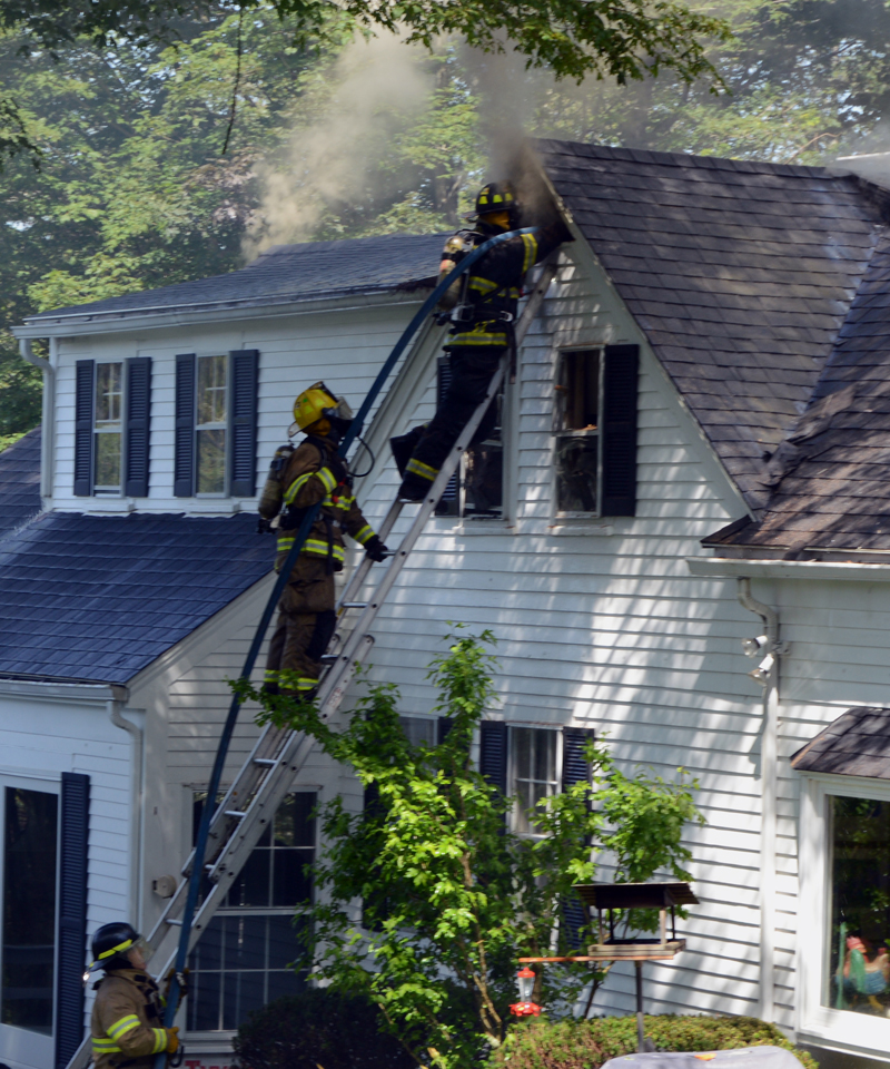 A firefighter attempts to douse the blaze at 26 Logan Road in Boothbay Harbor from the front side of the house after cutting a triangular hole in the attic wall with a chainsaw. (Evan Houk photo)